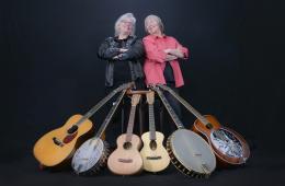 photo of Cathy and Marcy smiling and standing with arms folded behind guitars and other string instruments