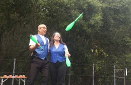 photo of two people dressed in blue vests and white shirts juggling green juggling pins