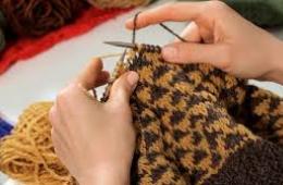 Two hands knitting a yellow scarf. 