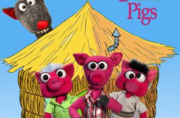 photo of three little pig puppets in front of a cartoon house with the big bad wolf puppet behind them