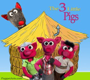 photo of three little pig puppets in front of a cartoon house with the big bad wolf puppet behind them