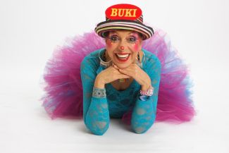 photo of Buki laying on floor with red hat on head that has her name written in yellow letters, a turquoise top, and a purple and blue tutu
